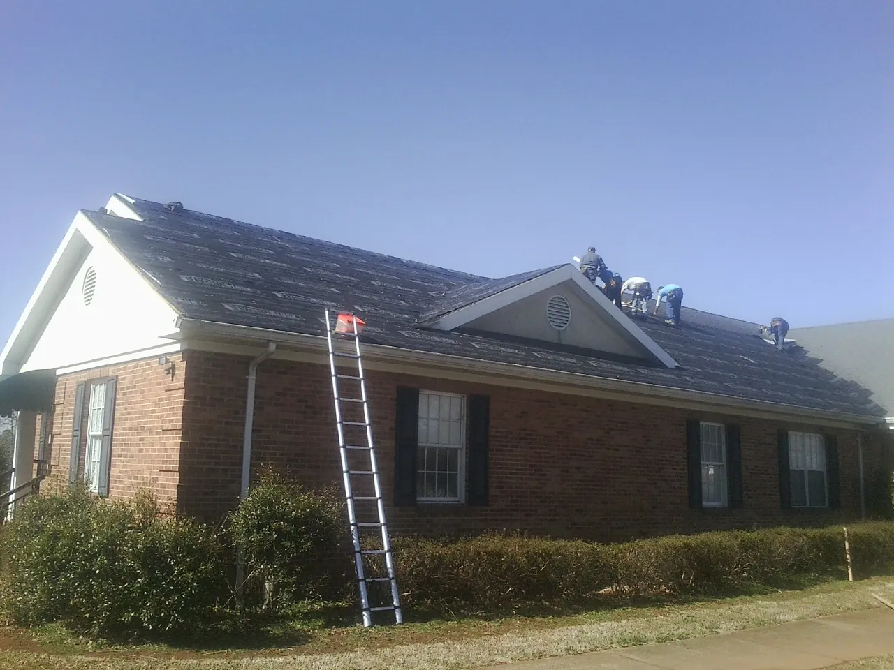 Crew tearing shingles off a brick ranch roof with a ladder set — Emergency Roof Repair work by our crew in Banks