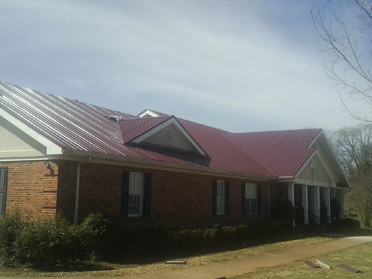 Red metal roof with gabled entries on a long brick building, from a Hail Damage Roof Repair job in Banks