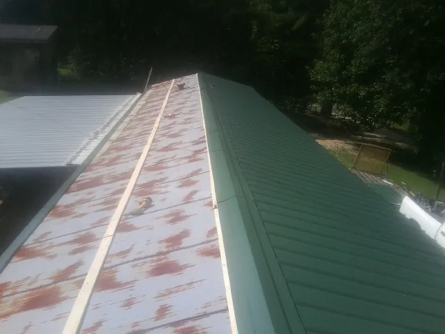 Old rusted panels beside newly installed green metal roofing — Wind Damage Roof Repair by Roofing Brothers in Banks