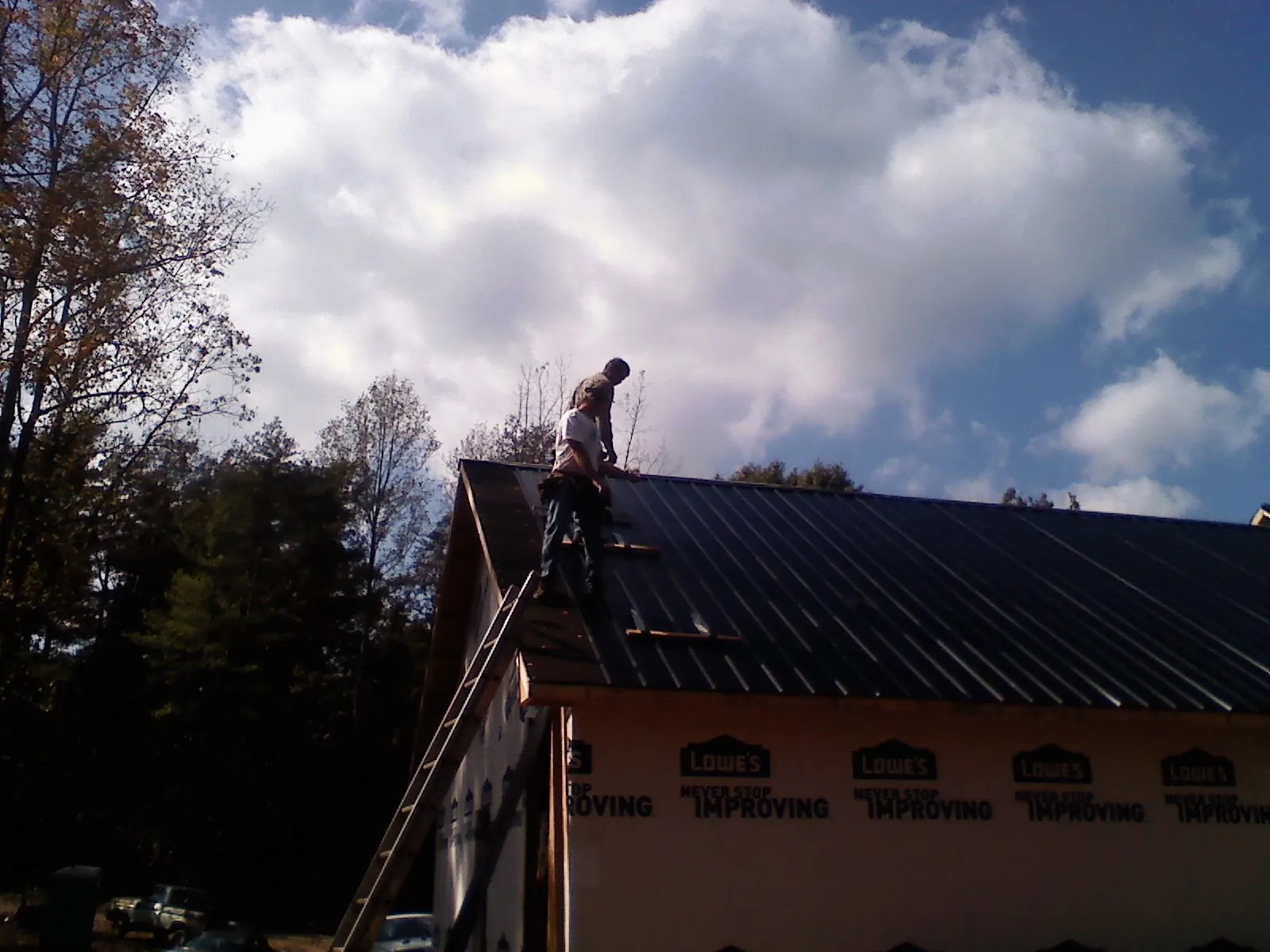 Roofer fastening dark metal panels high against a cloudy sky, from a Roof Inspection job in Banks